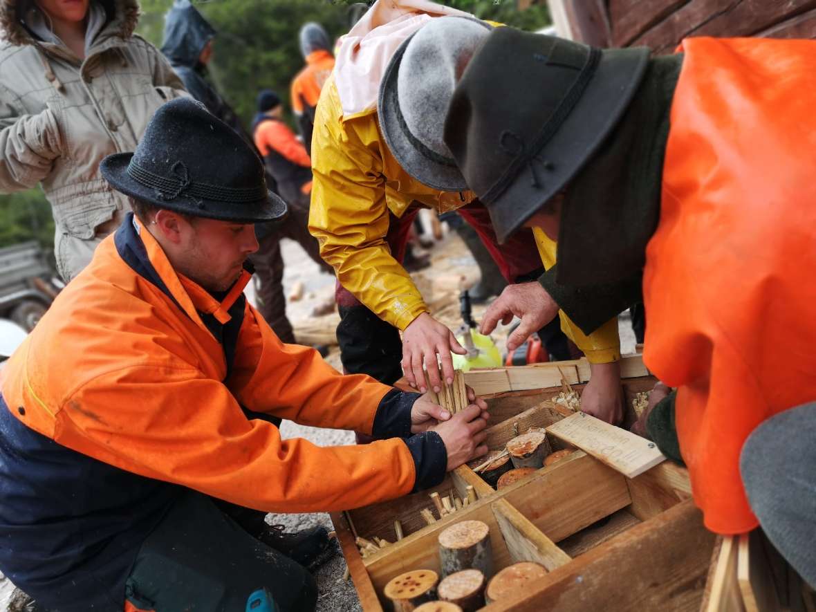 Schüler arbeiten in grün-oranger Arbeitskleidung an Insektenhotel